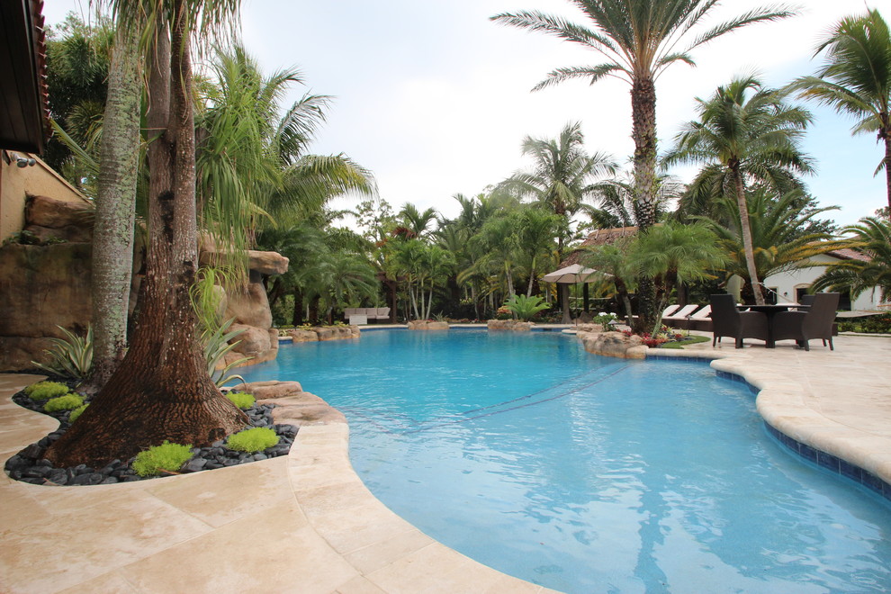 Large tropical backyard kidney-shaped natural pool in Miami with a water slide and natural stone pavers.