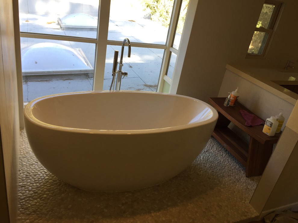Inspiration for a large modern master bathroom in Los Angeles with flat-panel cabinets, medium wood cabinets, a freestanding tub, a corner shower, a one-piece toilet, beige tile, porcelain tile, beige walls, pebble tile floors, an undermount sink, copper benchtops and beige floor.