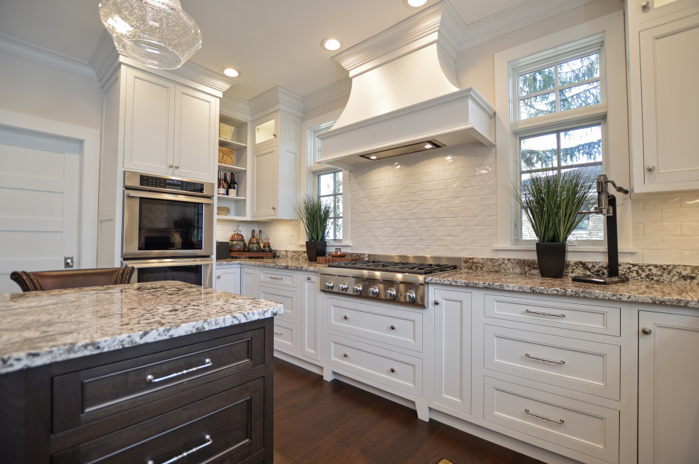 Inspiration for a transitional dark wood floor and brown floor eat-in kitchen remodel with an undermount sink, shaker cabinets, white cabinets, granite countertops, white backsplash, ceramic backsplash, stainless steel appliances, an island and beige countertops