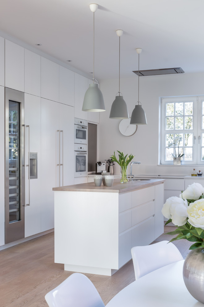 Photo of a scandinavian l-shaped kitchen in London with flat-panel cabinets, white cabinets, stainless steel appliances, light hardwood floors and with island.