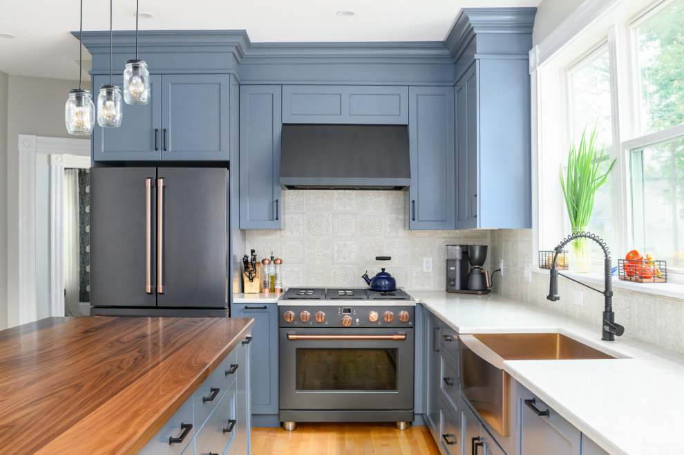 Inspiration for a mid-sized farmhouse l-shaped medium tone wood floor and brown floor eat-in kitchen remodel in Boston with a farmhouse sink, recessed-panel cabinets, blue cabinets, wood countertops, beige backsplash, ceramic backsplash, black appliances, an island and brown countertops