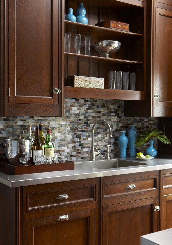 This is an example of a mid-sized traditional single-wall wet bar in New York with an integrated sink, beaded inset cabinets, dark wood cabinets, stainless steel benchtops, multi-coloured splashback and mosaic tile splashback.