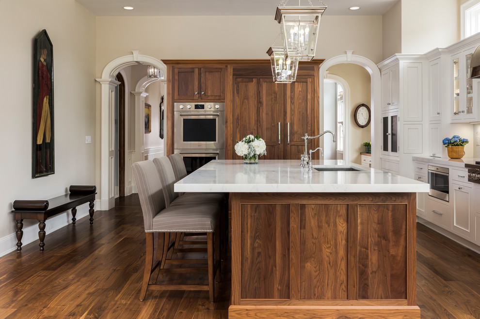 Traditional kitchen in New York with an undermount sink, recessed-panel cabinets, white cabinets, marble benchtops, white splashback, with island, brown floor, white benchtop, stainless steel appliances and dark hardwood floors.