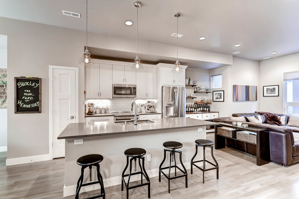Large contemporary single-wall open plan kitchen in Denver with a double-bowl sink, shaker cabinets, white cabinets, limestone benchtops, white splashback, subway tile splashback, stainless steel appliances, light hardwood floors, with island, beige floor and grey benchtop.