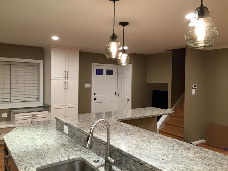 Example of a large transitional galley light wood floor open concept kitchen design in DC Metro with an undermount sink, recessed-panel cabinets, white cabinets, granite countertops, beige backsplash, white appliances and an island