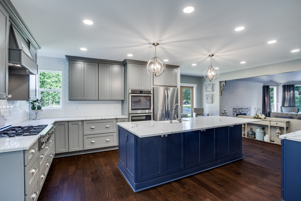 Large transitional l-shaped eat-in kitchen in Portland with a farmhouse sink, shaker cabinets, grey cabinets, quartz benchtops, white splashback, ceramic splashback, stainless steel appliances, plywood floors, with island, brown floor and white benchtop.