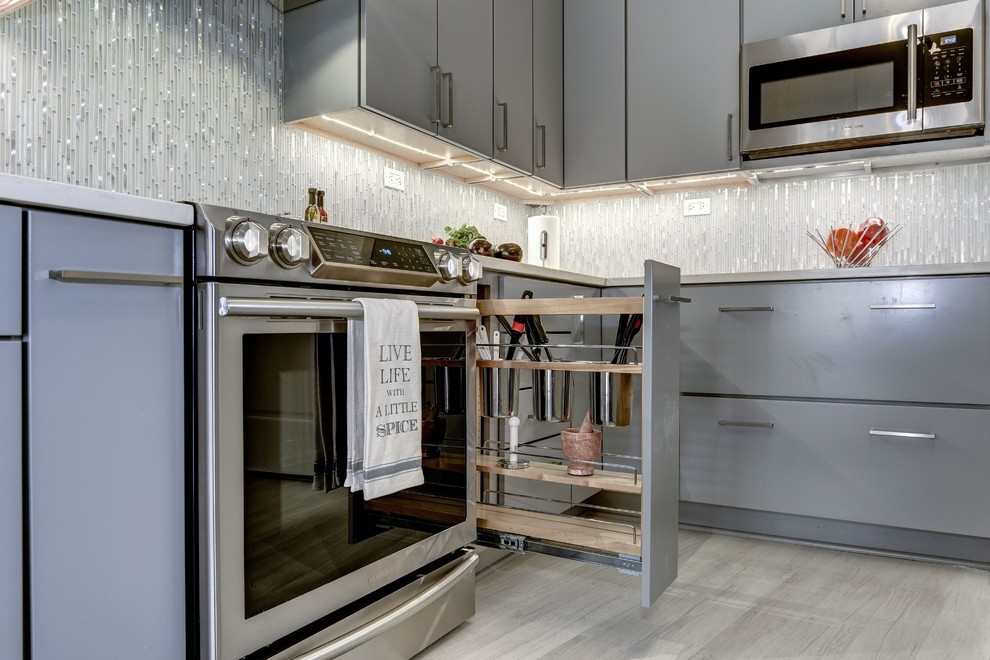 This is an example of a mid-sized contemporary l-shaped eat-in kitchen in DC Metro with a single-bowl sink, flat-panel cabinets, grey cabinets, quartz benchtops, yellow splashback, glass tile splashback, stainless steel appliances, laminate floors, with island and white floor.