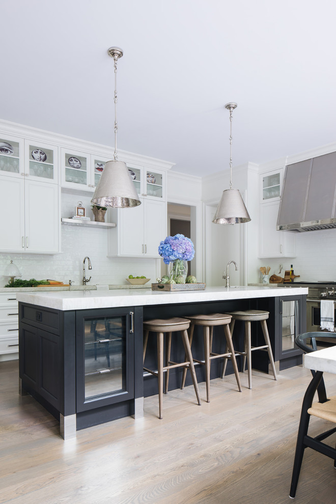 This is an example of a transitional eat-in kitchen in Chicago with white cabinets, white splashback, ceramic splashback, stainless steel appliances, medium hardwood floors, with island and white benchtop.