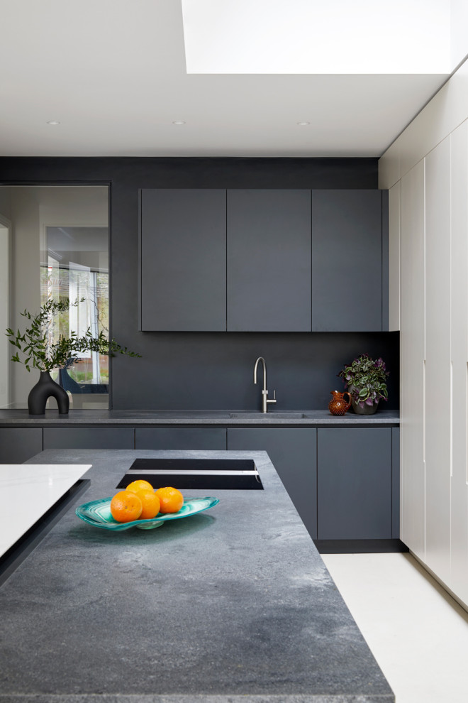 Photo of an expansive contemporary kitchen in London with flat-panel cabinets, black cabinets, composite countertops, multiple islands, grey worktops, a built-in sink, black splashback, granite splashback, concrete flooring and beige floors.