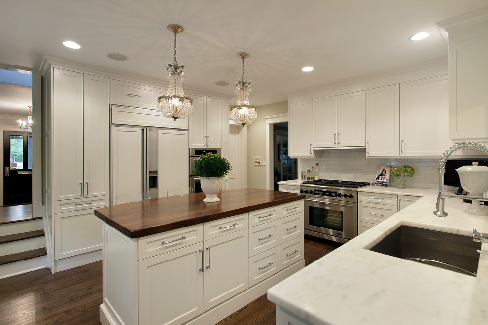 This is an example of a traditional u-shaped kitchen in Chicago with an undermount sink, shaker cabinets, beige cabinets, wood benchtops, beige splashback, subway tile splashback and panelled appliances.