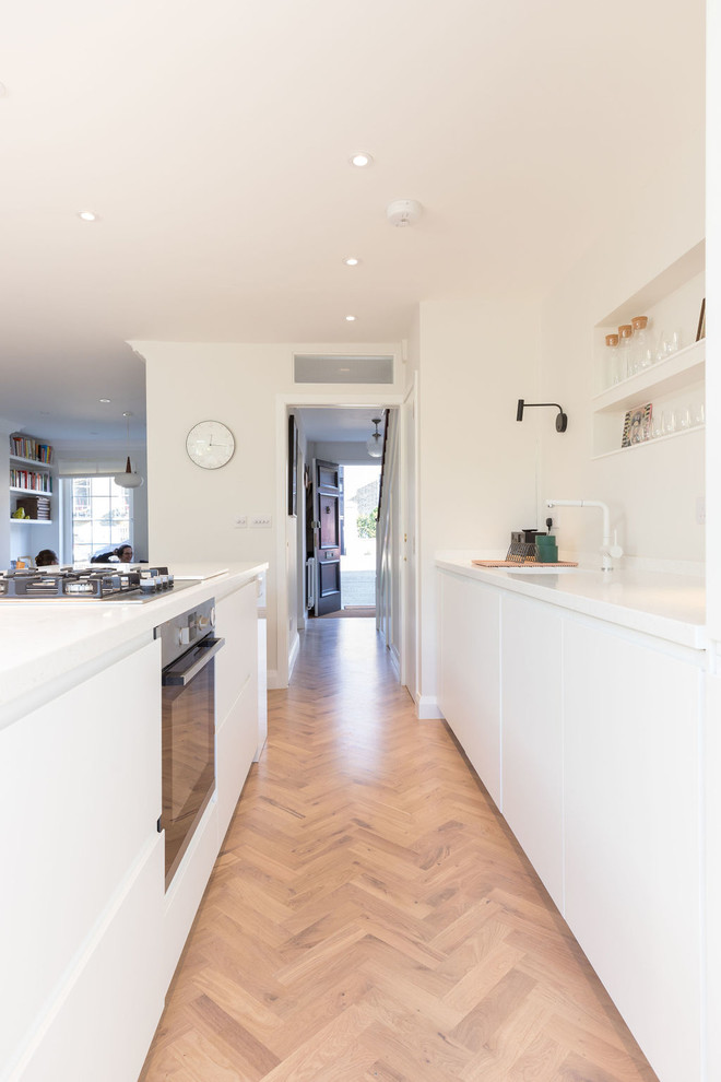 Photo of a medium sized contemporary single-wall open plan kitchen in London with flat-panel cabinets, white cabinets, composite countertops, light hardwood flooring, an island, brown floors, white worktops and integrated appliances.