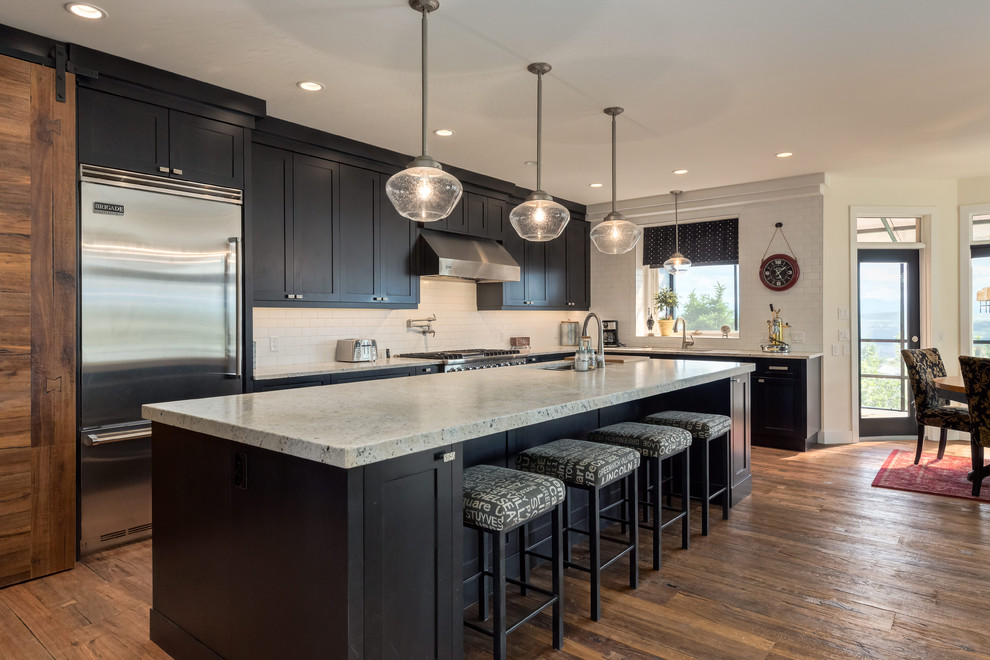 Inspiration for a transitional u-shaped medium tone wood floor and brown floor kitchen remodel in Calgary with an undermount sink, shaker cabinets, black cabinets, quartz countertops, white backsplash, ceramic backsplash, stainless steel appliances and an island