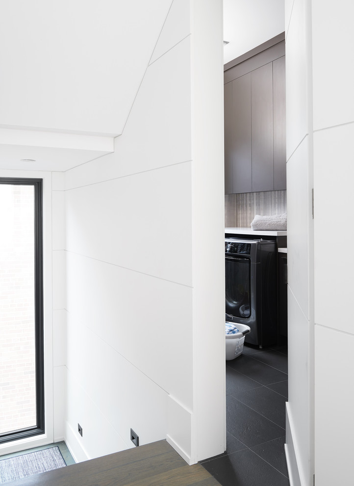 Photo of a mid-sized contemporary galley dedicated laundry room in Toronto with an integrated sink, flat-panel cabinets, dark wood cabinets, quartzite benchtops, white walls, porcelain floors, an integrated washer and dryer, black floor and white benchtop.