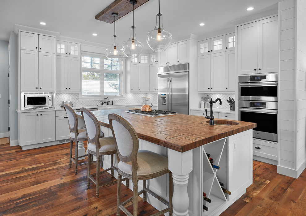 Inspiration for a country l-shaped kitchen in Edmonton with shaker cabinets, white cabinets, white splashback, stainless steel appliances, dark hardwood floors, with island and brown floor.