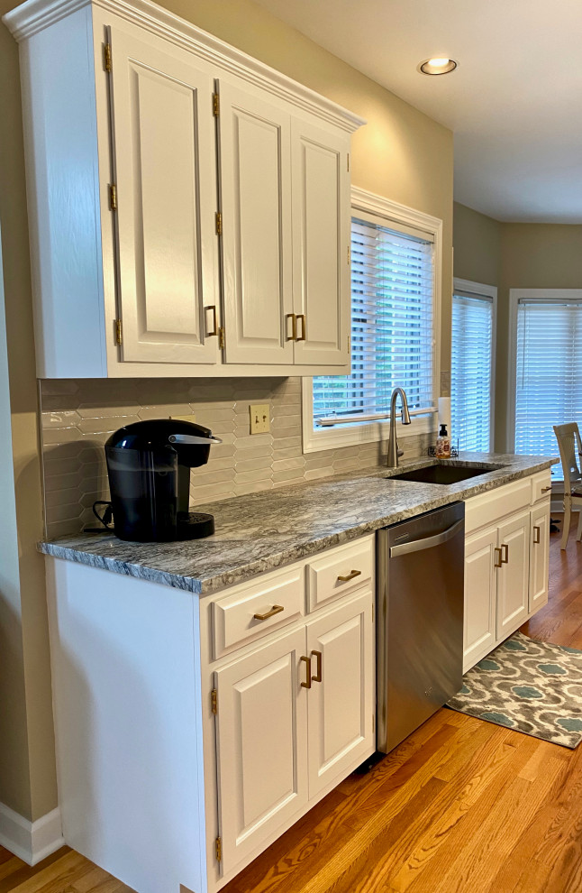 This is an example of a mid-sized transitional u-shaped eat-in kitchen in Chicago with an undermount sink, flat-panel cabinets, white cabinets, granite benchtops, grey splashback, granite splashback, stainless steel appliances, light hardwood floors, with island, brown floor and grey benchtop.