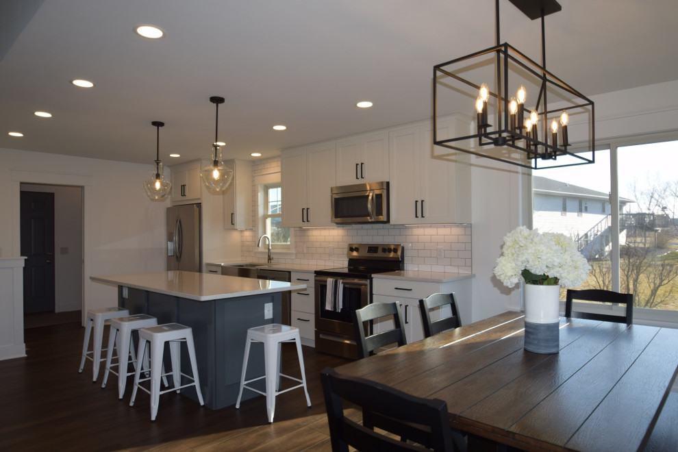 Mid-sized transitional single-wall vinyl floor open concept kitchen photo with a farmhouse sink, shaker cabinets, quartz countertops, white backsplash, subway tile backsplash, stainless steel appliances, an island and white countertops