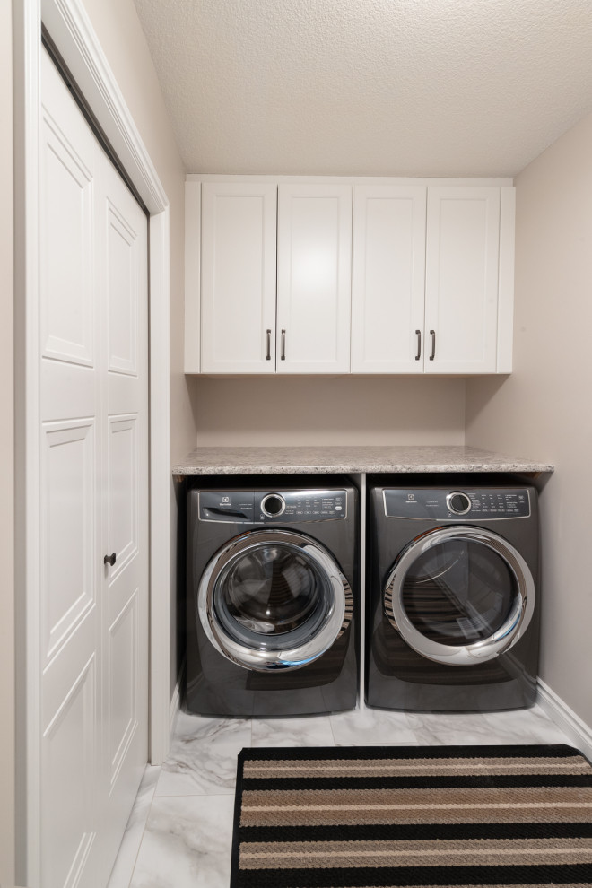 Photo of a small traditional galley utility room in Edmonton with shaker cabinets, white cabinets, granite worktops, beige walls, ceramic flooring, a side by side washer and dryer, white floors and grey worktops.