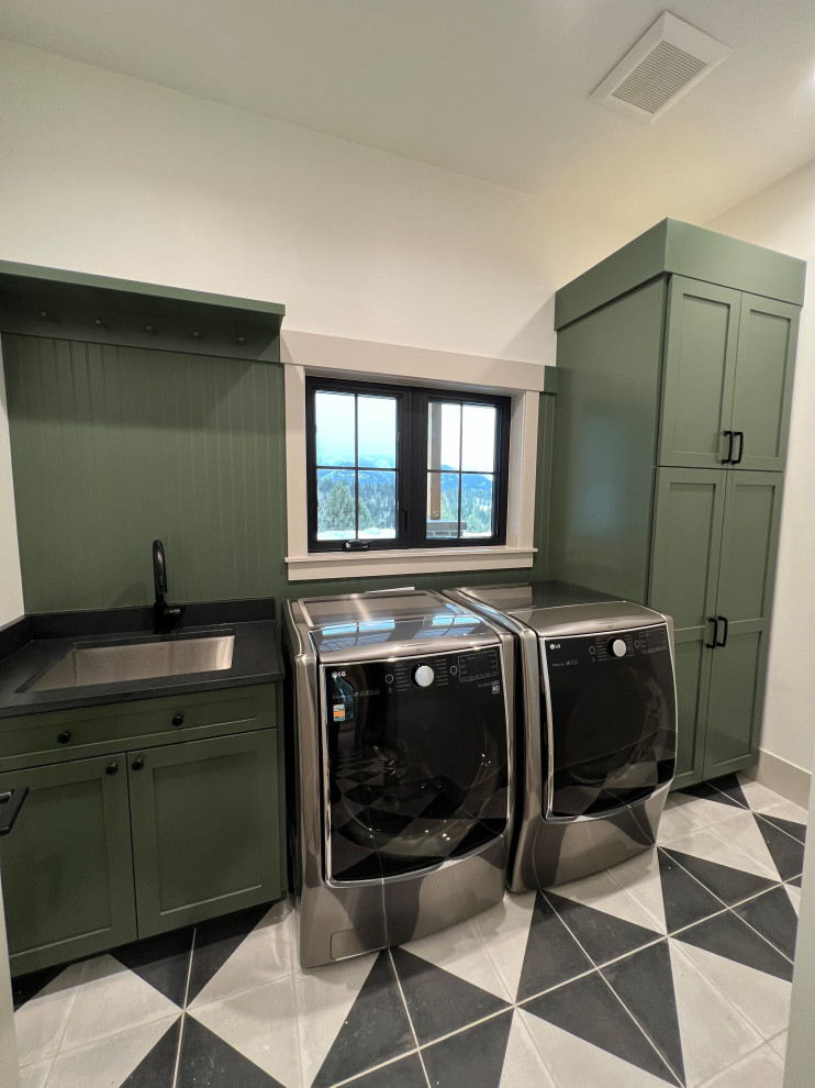 他の地域にある高級な中くらいなトランジショナルスタイルのおしゃれな洗濯室 (シェーカースタイル扉のキャビネット、アンダーカウンターシンク、緑のキャビネット、クオーツストーンカウンター、緑のキッチンパネル、木材のキッチンパネル、ベージュの壁、セラミックタイルの床、左右配置の洗濯機・乾燥機、黒いキッチンカウンター) の写真