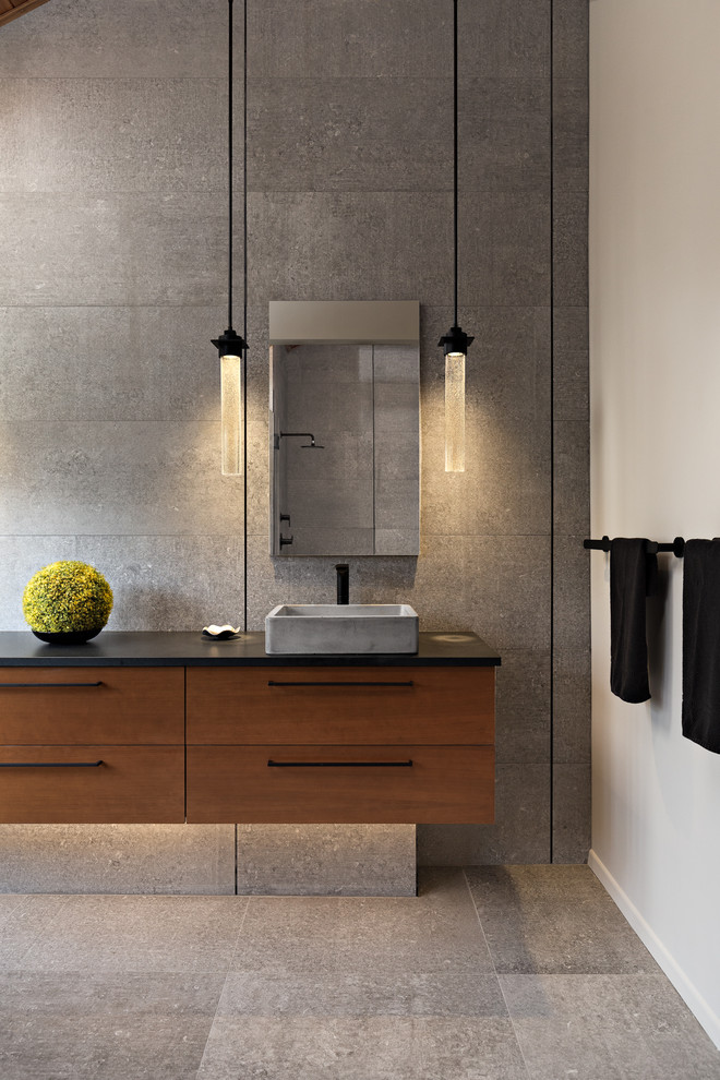 This is an example of a large contemporary master bathroom in Other with flat-panel cabinets, medium wood cabinets, a double shower, a one-piece toilet, gray tile, grey walls, a vessel sink, grey floor, a hinged shower door, black benchtops, concrete floors and concrete benchtops.