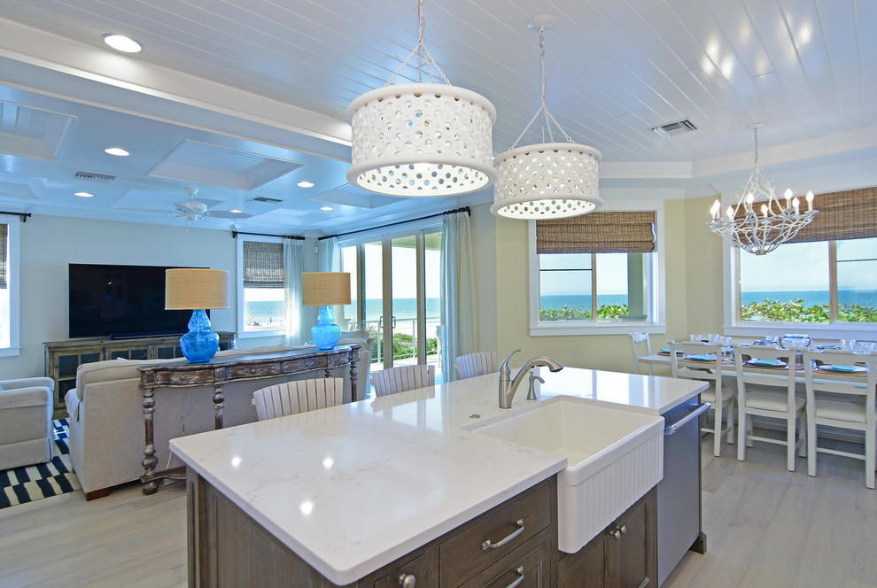Inspiration for a mid-sized beach style single-wall eat-in kitchen in Tampa with a farmhouse sink, recessed-panel cabinets, white cabinets, glass tile splashback, stainless steel appliances, light hardwood floors, with island, quartzite benchtops and white splashback.