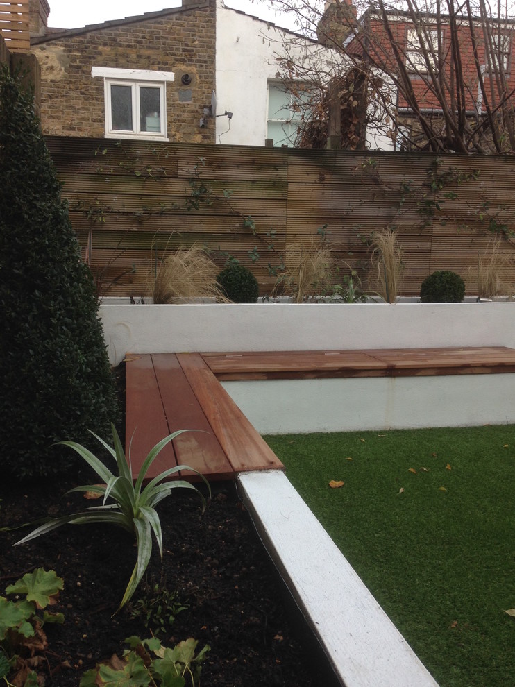 Small modern backyard full sun formal garden in London with a container garden and decking for summer.