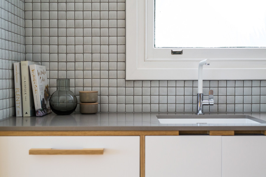 This is an example of a small scandinavian l-shaped eat-in kitchen in Adelaide with an undermount sink, flat-panel cabinets, white cabinets, solid surface benchtops, grey splashback, ceramic splashback, white appliances, medium hardwood floors, with island, brown floor and grey benchtop.