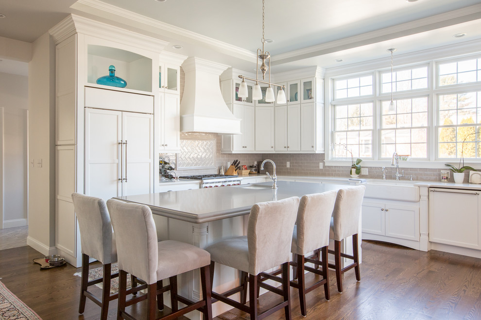 Inspiration for a large transitional l-shaped open plan kitchen in Providence with a farmhouse sink, recessed-panel cabinets, white cabinets, beige splashback, subway tile splashback, panelled appliances, with island, dark hardwood floors and quartz benchtops.