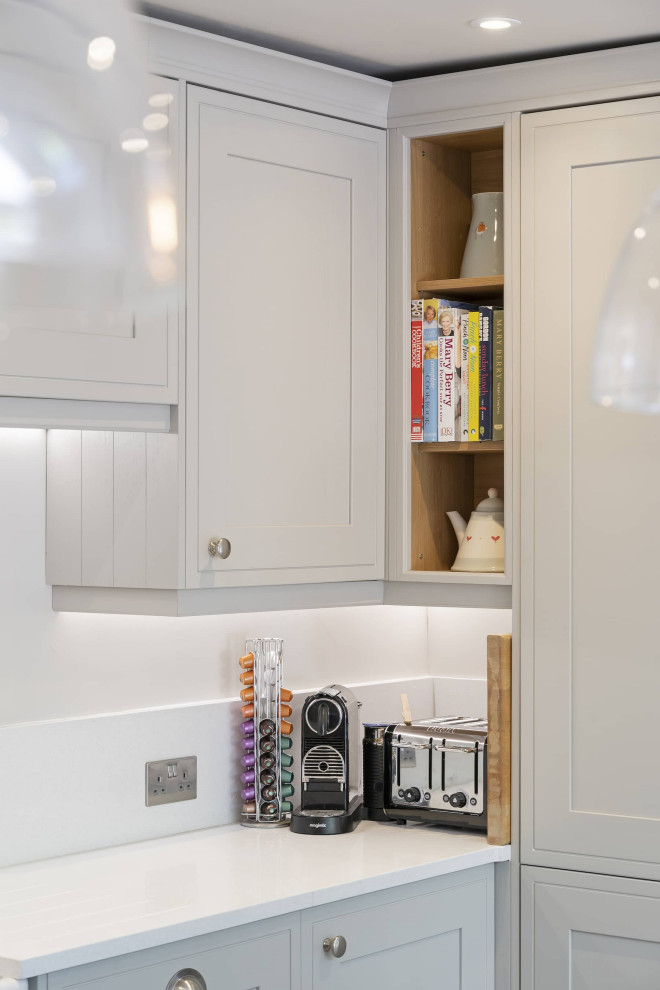 Inspiration for a mid-sized traditional l-shaped open plan kitchen in Oxfordshire with a double-bowl sink, shaker cabinets, white cabinets, quartzite benchtops, white splashback, ceramic splashback, black appliances, ceramic floors, with island, brown floor and white benchtop.
