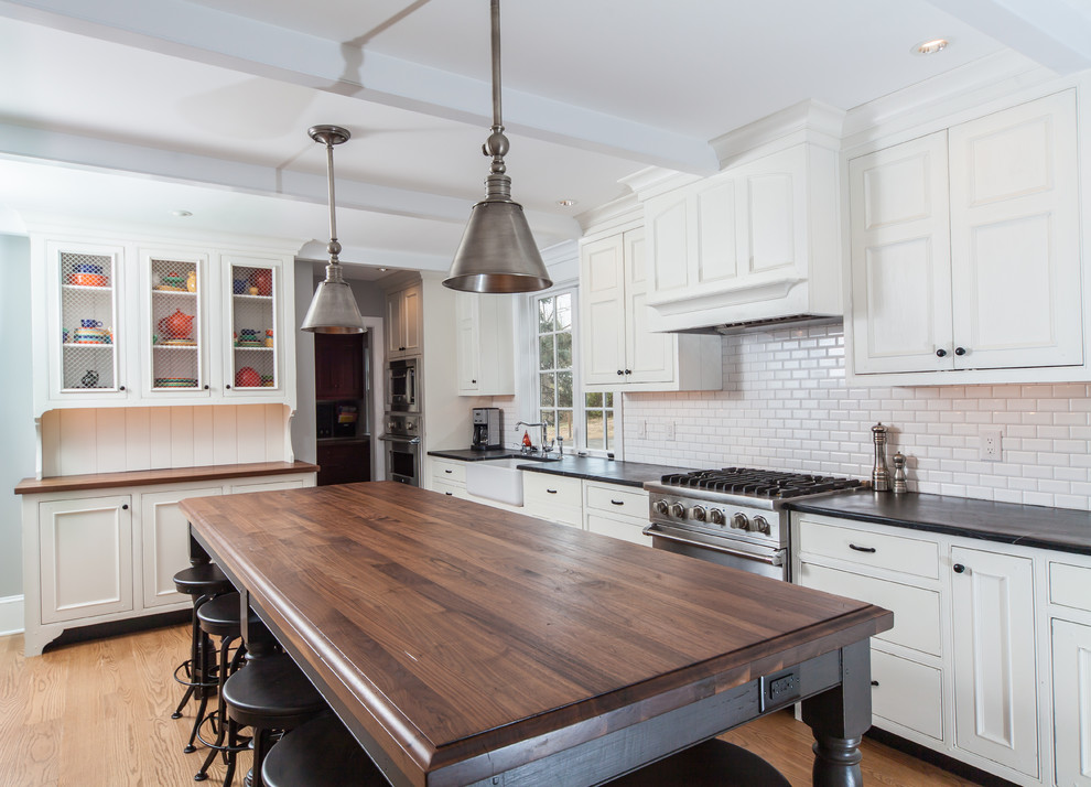 This is an example of a large transitional l-shaped eat-in kitchen in Philadelphia with a single-bowl sink, white splashback, subway tile splashback, stainless steel appliances, recessed-panel cabinets, white cabinets, light hardwood floors, with island, brown floor, soapstone benchtops and black benchtop.