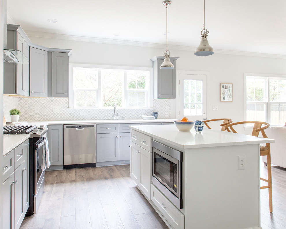 Beach style open plan kitchen in Charlotte with an undermount sink, shaker cabinets, white splashback, stainless steel appliances, medium hardwood floors, with island, brown floor and white benchtop.
