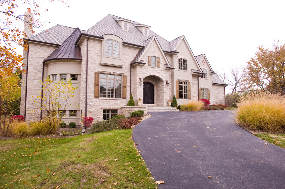 Photo of an expansive traditional two-storey beige house exterior in Chicago with stone veneer and a shingle roof.