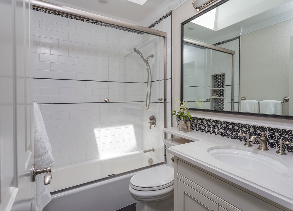 Design ideas for a small bathroom in San Francisco with shaker cabinets, white cabinets, an undermount tub, a shower/bathtub combo, a one-piece toilet, black tile, porcelain tile, white walls, porcelain floors, an undermount sink, engineered quartz benchtops, black floor, a sliding shower screen and white benchtops.
