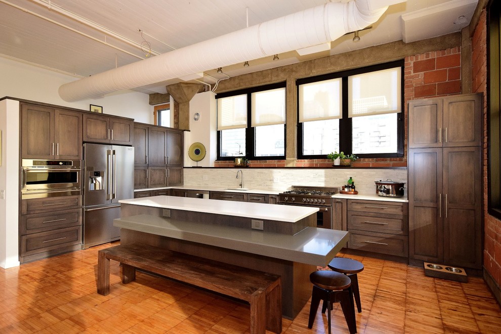 Inspiration for a large industrial u-shaped eat-in kitchen in Chicago with a drop-in sink, recessed-panel cabinets, dark wood cabinets, granite benchtops, white splashback, terra-cotta splashback, stainless steel appliances, medium hardwood floors, with island and brown floor.