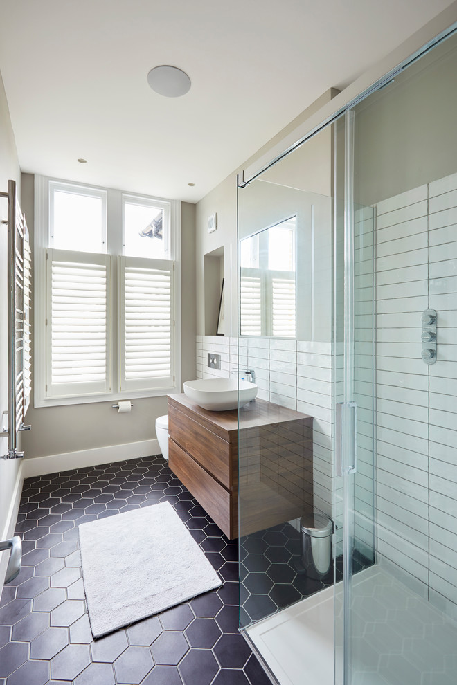 This is an example of a mid-sized contemporary 3/4 bathroom in London with flat-panel cabinets, brown cabinets, an open shower, a wall-mount toilet, white tile, ceramic tile, green walls, ceramic floors, a vessel sink, wood benchtops, black floor, a sliding shower screen and brown benchtops.