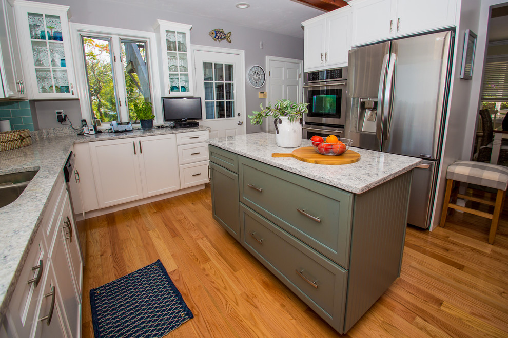 This is an example of a mid-sized beach style u-shaped eat-in kitchen in Boston with flat-panel cabinets, white cabinets, quartz benchtops, blue splashback, glass tile splashback, stainless steel appliances, with island, white benchtop, an undermount sink, medium hardwood floors and brown floor.