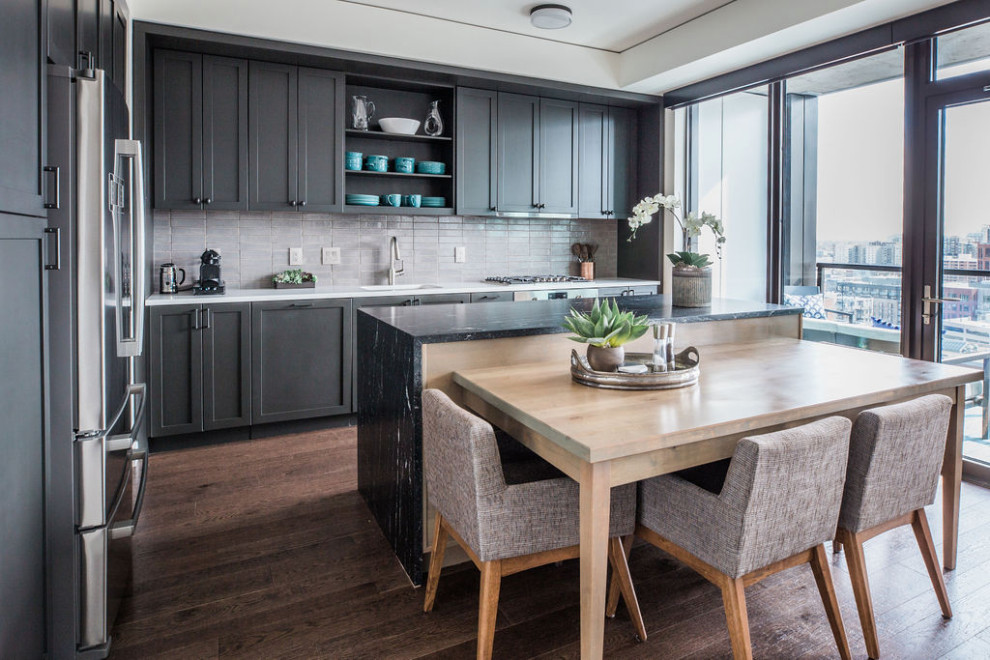 Mid-sized transitional l-shaped eat-in kitchen in Denver with shaker cabinets, grey splashback, ceramic splashback, stainless steel appliances, with island, brown floor, a single-bowl sink, black cabinets, dark hardwood floors and white benchtop.