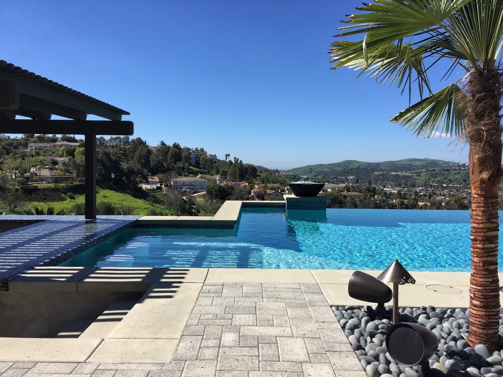 This is an example of a large contemporary backyard rectangular infinity pool in Los Angeles with a hot tub and concrete pavers.