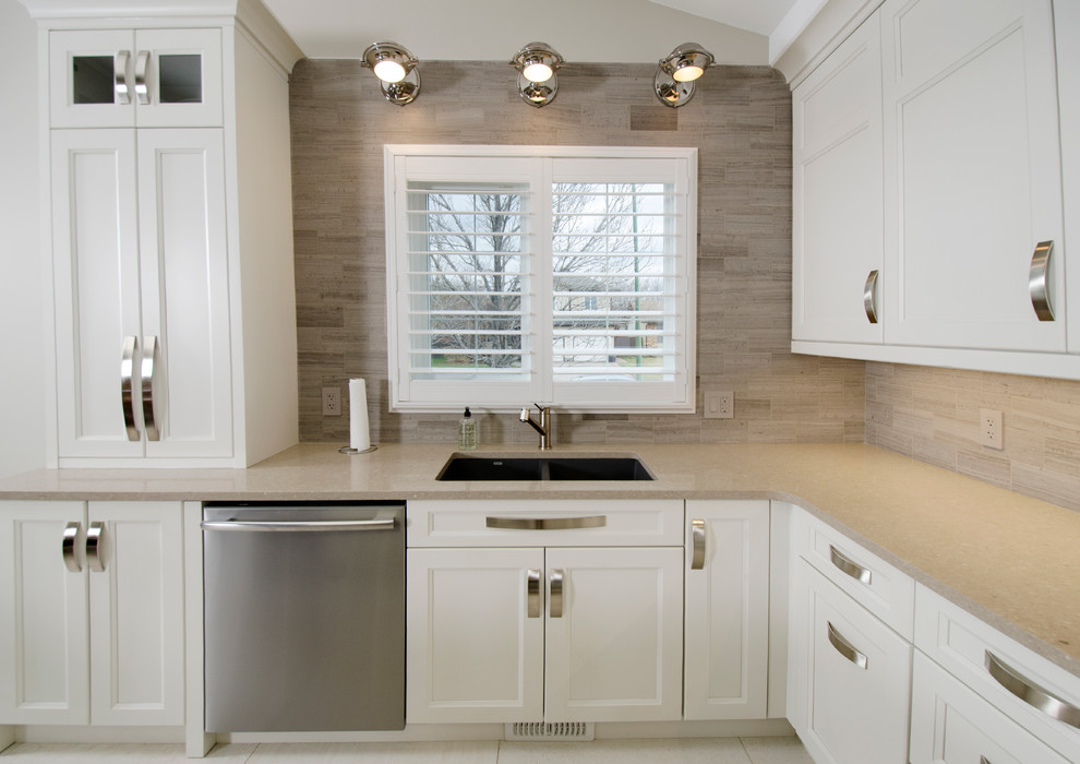Example of a transitional u-shaped limestone floor eat-in kitchen design with an undermount sink, raised-panel cabinets, gray cabinets, quartz countertops, beige backsplash, stone tile backsplash, stainless steel appliances and an island