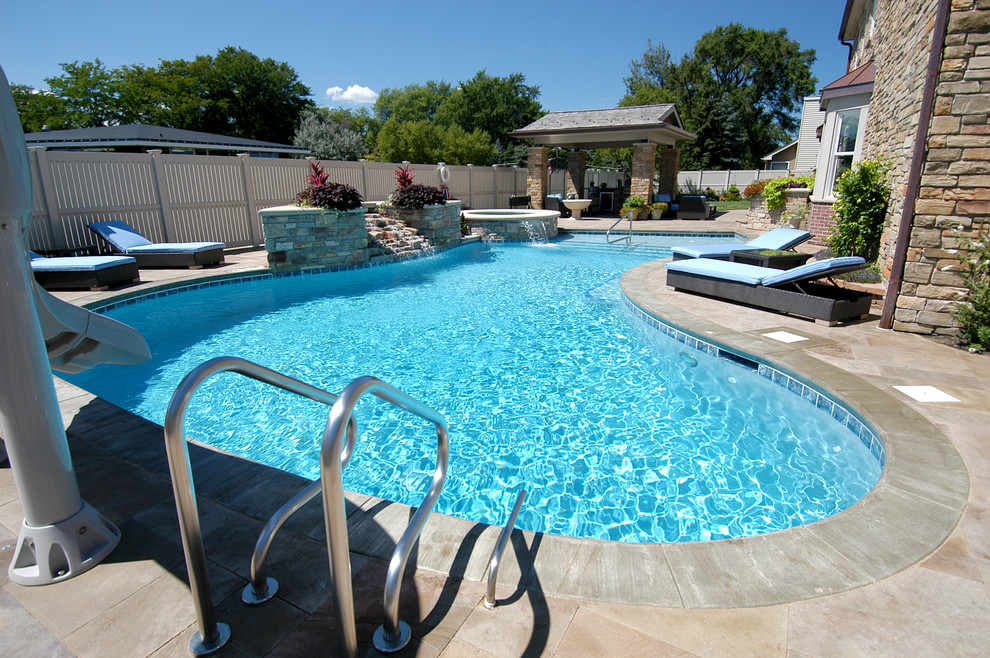Photo of a mid-sized traditional backyard custom-shaped natural pool in Chicago with a hot tub and natural stone pavers.