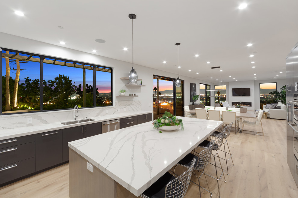 This is an example of a large contemporary u-shaped eat-in kitchen in Los Angeles with an undermount sink, stainless steel appliances, with island, quartz benchtops, white splashback, stone slab splashback, light hardwood floors and white benchtop.