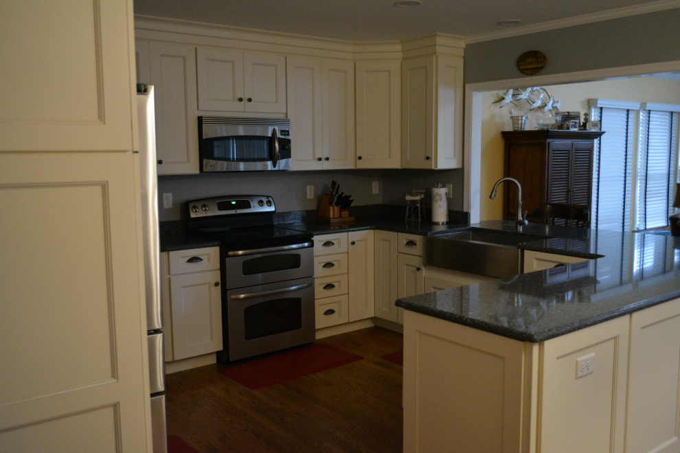 Mid-sized transitional u-shaped dark wood floor and brown floor eat-in kitchen photo with a farmhouse sink, shaker cabinets, beige cabinets, granite countertops, gray backsplash, mosaic tile backsplash, stainless steel appliances, a peninsula and black countertops