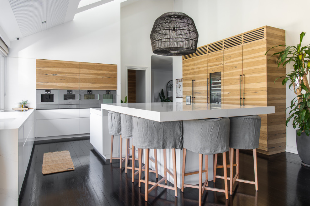 Inspiration for a contemporary u-shaped kitchen in Sydney with flat-panel cabinets, medium wood cabinets, stainless steel appliances, dark hardwood floors, with island, brown floor and white benchtop.