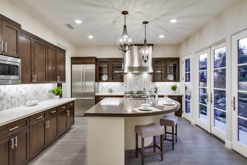 This is an example of a mid-sized transitional u-shaped separate kitchen in San Diego with a farmhouse sink, recessed-panel cabinets, dark wood cabinets, quartz benchtops, grey splashback, stainless steel appliances, porcelain floors, with island, grey floor, ceramic splashback and white benchtop.