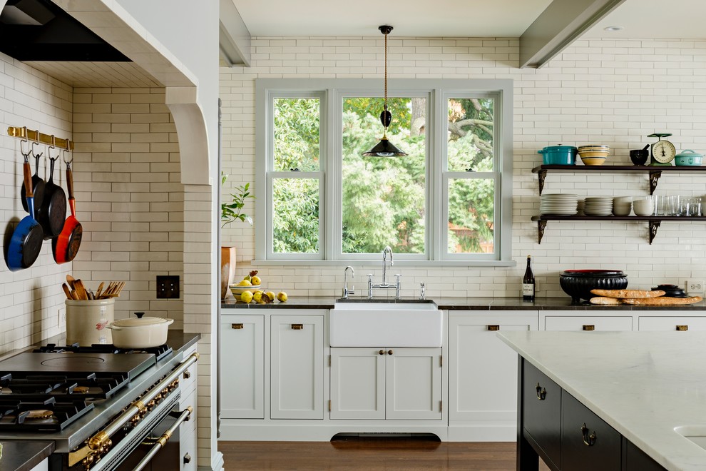 Inspiration for a large country l-shaped eat-in kitchen in Portland with a farmhouse sink, white cabinets, marble benchtops, white splashback, subway tile splashback, flat-panel cabinets, black appliances, dark hardwood floors and with island.