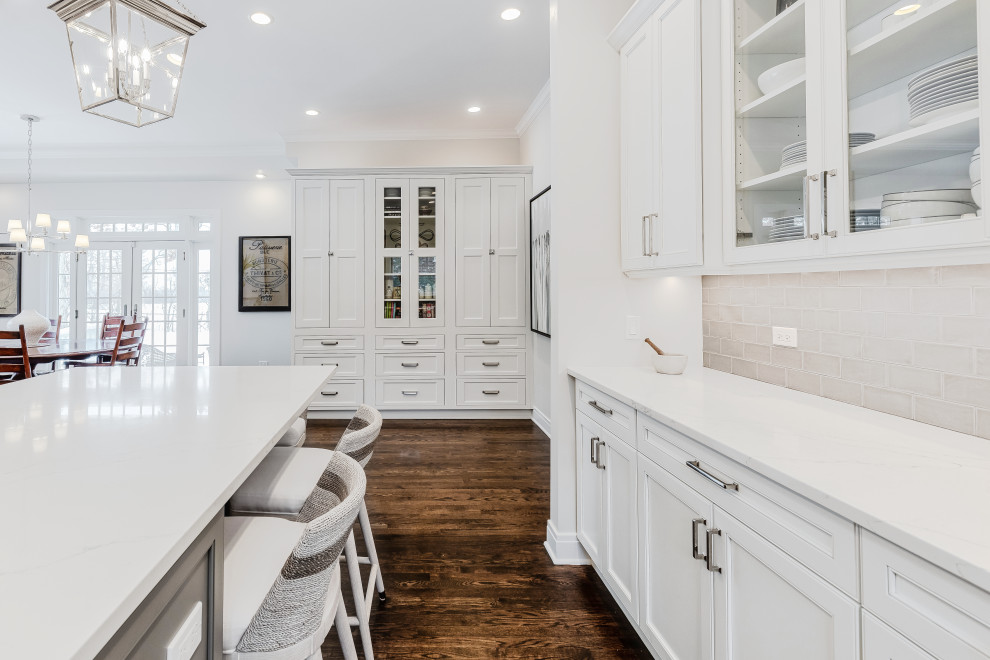 Design ideas for a large classic u-shaped kitchen/diner in Chicago with beaded cabinets, white cabinets, engineered stone countertops, grey splashback, glass tiled splashback, stainless steel appliances, an island, white worktops, a belfast sink, dark hardwood flooring and brown floors.