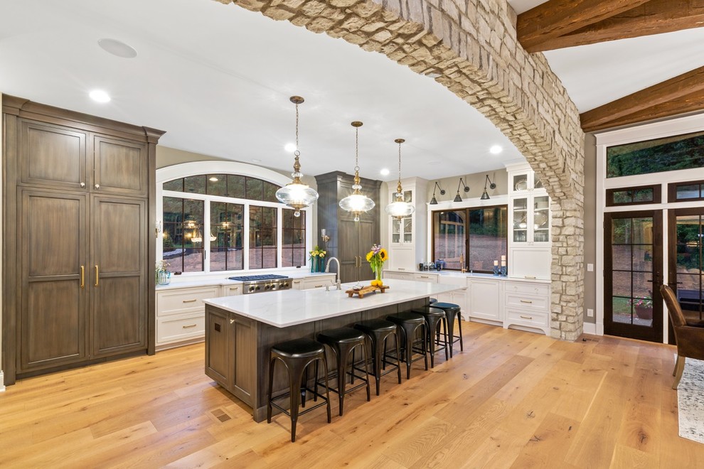 Large transitional l-shaped light wood floor eat-in kitchen photo in Cincinnati with a farmhouse sink, glass-front cabinets, medium tone wood cabinets, quartz countertops, paneled appliances, an island and white countertops