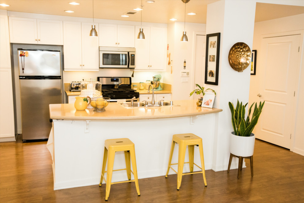 Mid-sized transitional galley dark wood floor and brown floor open concept kitchen photo in Orange County with a double-bowl sink, shaker cabinets, white cabinets, solid surface countertops, stainless steel appliances and a peninsula
