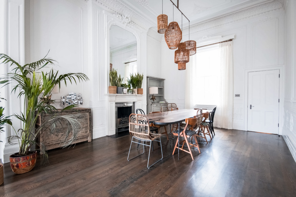 Large eclectic separate dining room in London with white walls, a standard fireplace, a plaster fireplace surround, dark hardwood floors and brown floor.