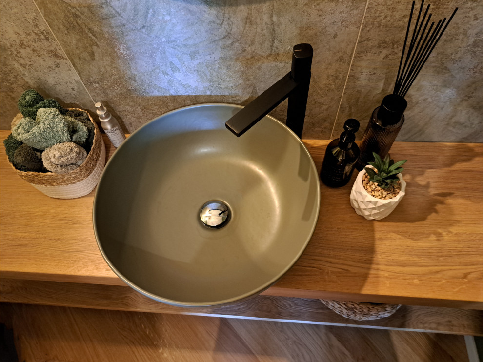 Modern inredning av ett mellanstort toalett, med skåp i ljust trä, en vägghängd toalettstol, grön kakel, porslinskakel, gröna väggar, ljust trägolv, ett fristående handfat och träbänkskiva