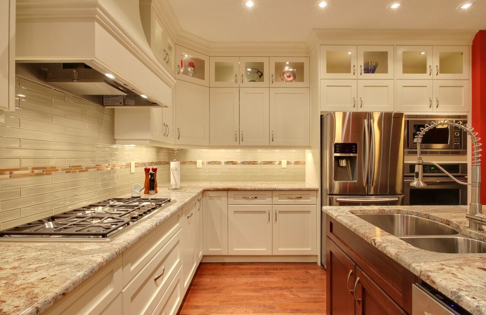 Large transitional l-shaped medium tone wood floor and brown floor open concept kitchen photo in Calgary with an undermount sink, recessed-panel cabinets, white cabinets, glass countertops, beige backsplash, matchstick tile backsplash, stainless steel appliances and an island
